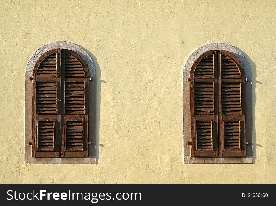 Two old brown wooden windows of the yellow wall