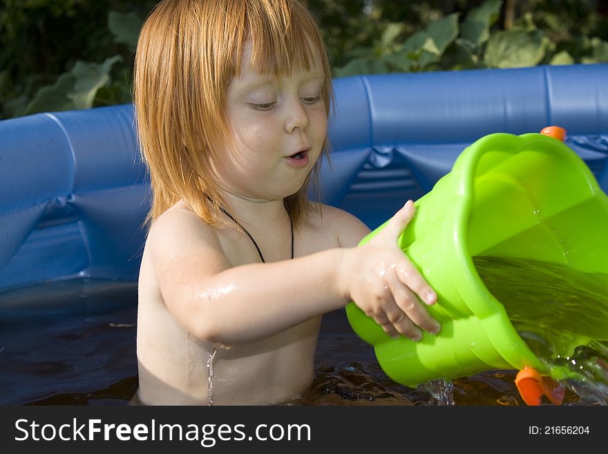 Happy child playing in a pool with green bucket.