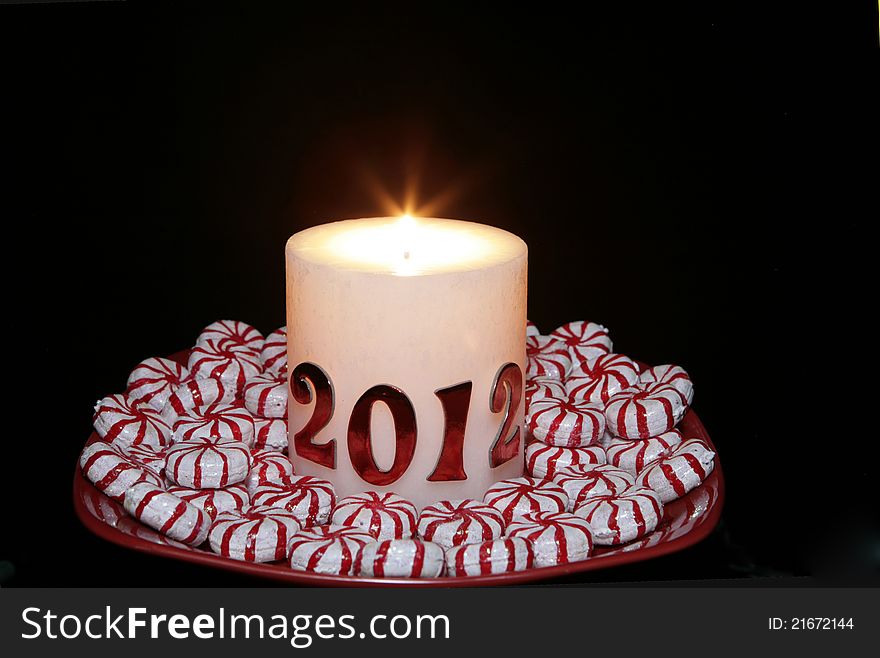 A 2012 Candle lit for the new year with peppermint candy placed around it on a red plate. A 2012 Candle lit for the new year with peppermint candy placed around it on a red plate.
