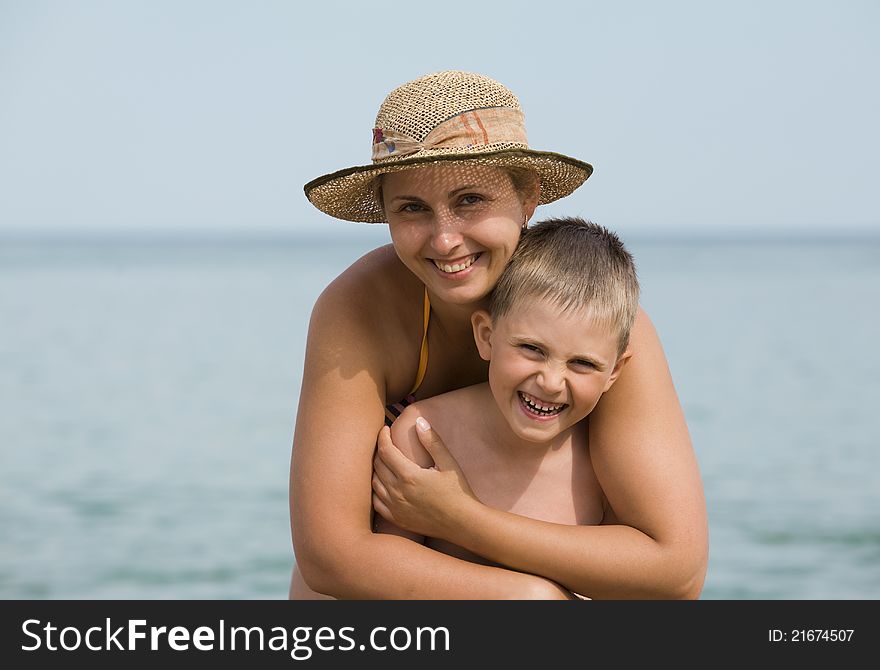 Mother embraces the son against the sea, both laugh. Mother embraces the son against the sea, both laugh