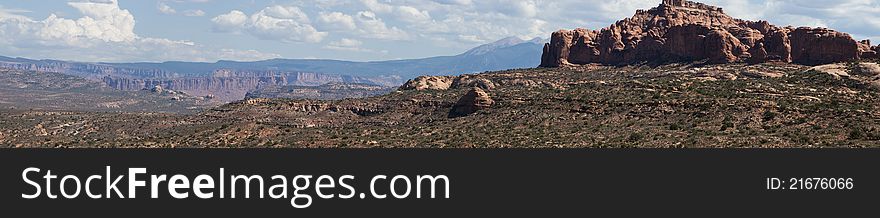 A super wide desert panorama with blue skies and red rocks.