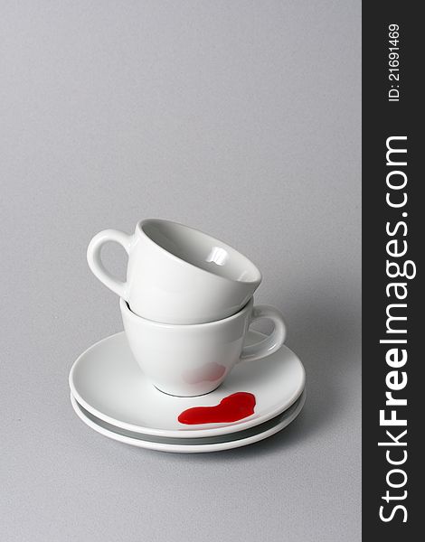 Two teacups neatly stacked for storage on a gray background with red, heart shaped tea puddle. Two teacups neatly stacked for storage on a gray background with red, heart shaped tea puddle