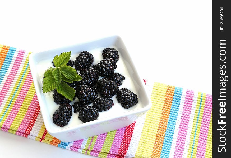 Blackberries on yogurt in a white, square, porcelain dish on a striped cloth. on a white background.