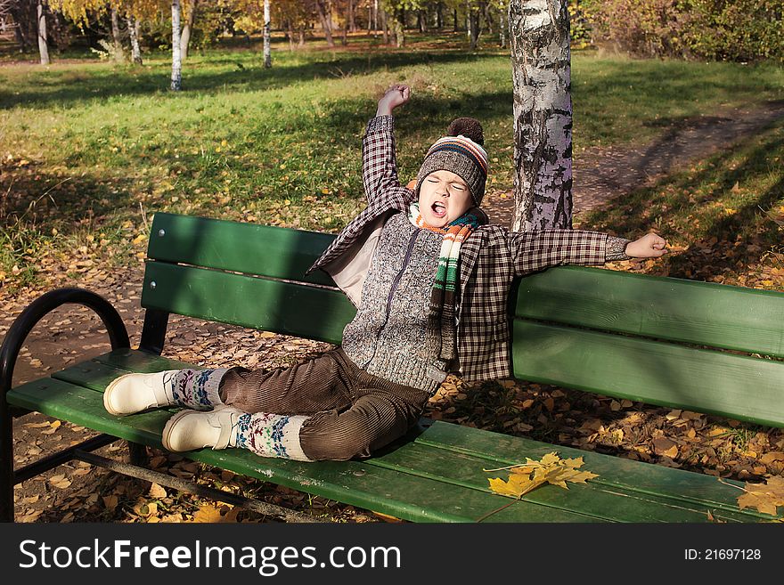 Boy stretching and yawning on park bench in autumn. Boy stretching and yawning on park bench in autumn.
