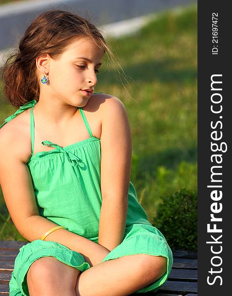 A girl sitting on a wooden bench outdoor in a green park. A girl sitting on a wooden bench outdoor in a green park