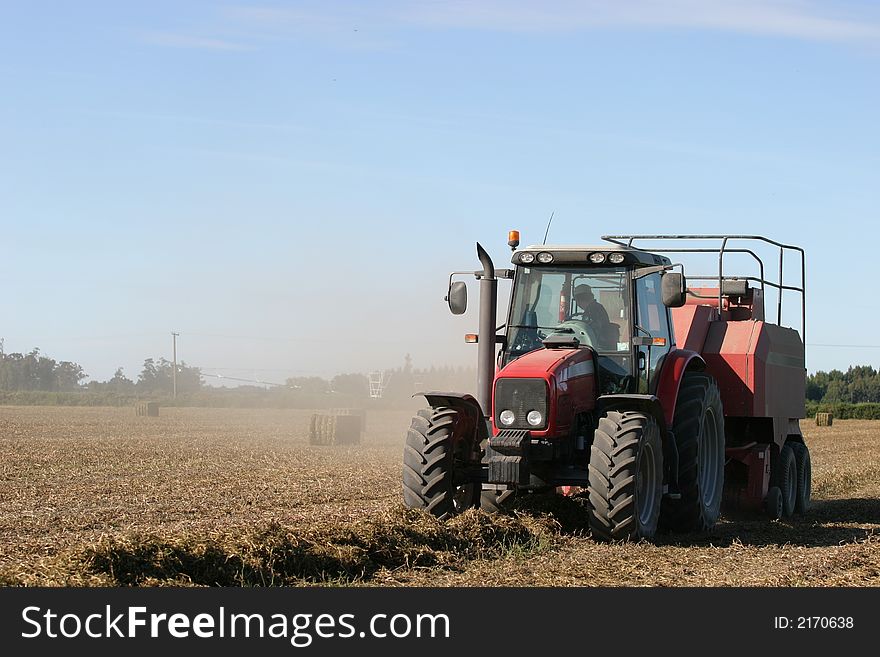 Tractor working to bale pea straw on the Canterbury Plains, New Zealand. Tractor working to bale pea straw on the Canterbury Plains, New Zealand