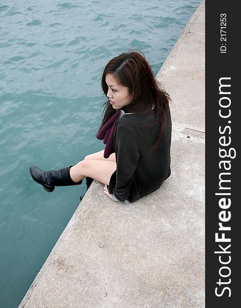 Asian girl sitting down on edge at pier dangling her legs. Asian girl sitting down on edge at pier dangling her legs