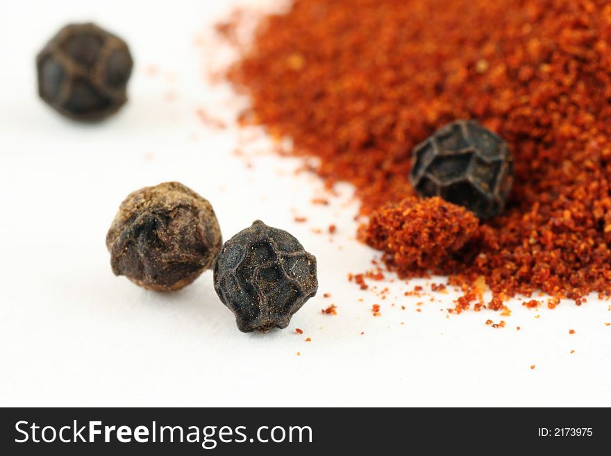 Close up of pepper corns and red hot chilli powder isolated on white - narrow focus. Close up of pepper corns and red hot chilli powder isolated on white - narrow focus