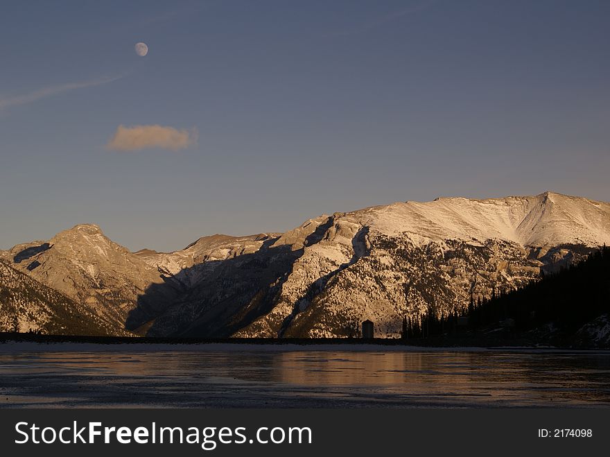 Fable & Grotto mountain at dusk in winter; Spray Lake in the foreground and moon in the background. Fable & Grotto mountain at dusk in winter; Spray Lake in the foreground and moon in the background.