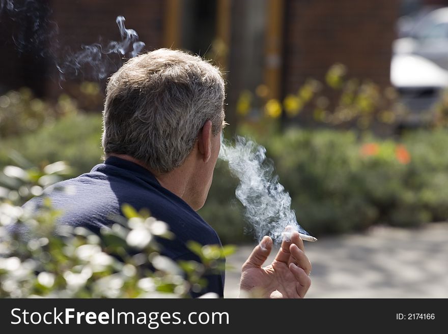 A man smoking a cigarette in the park. A man smoking a cigarette in the park