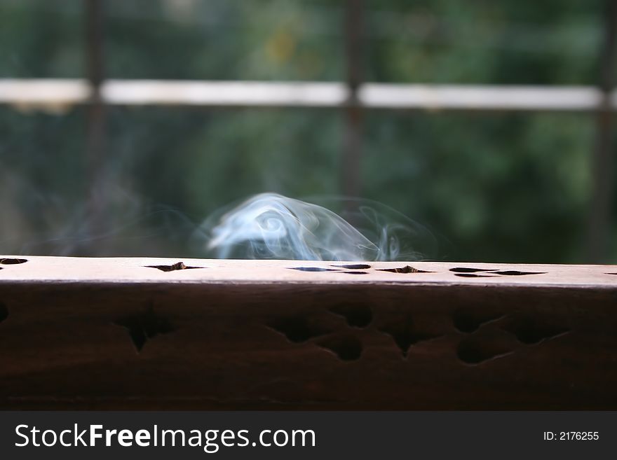 Incense smoke swirling out a wooden incense burner in the light