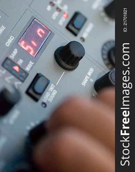 Detail of a red synthesizer front panel, with knobs and a hand tweaking them. Detail of a red synthesizer front panel, with knobs and a hand tweaking them.