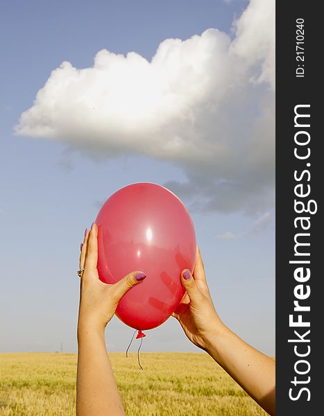 Woman hands holding red balloon. Agricultural field and sky with clouds in background. Woman hands holding red balloon. Agricultural field and sky with clouds in background.