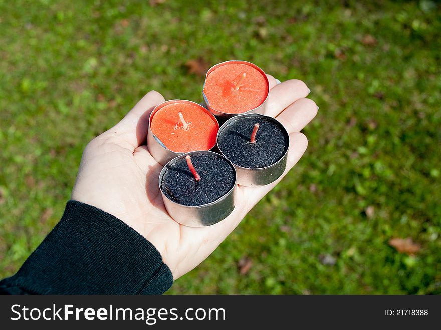 Hand holding black and orange tealights, outside. Hand holding black and orange tealights, outside