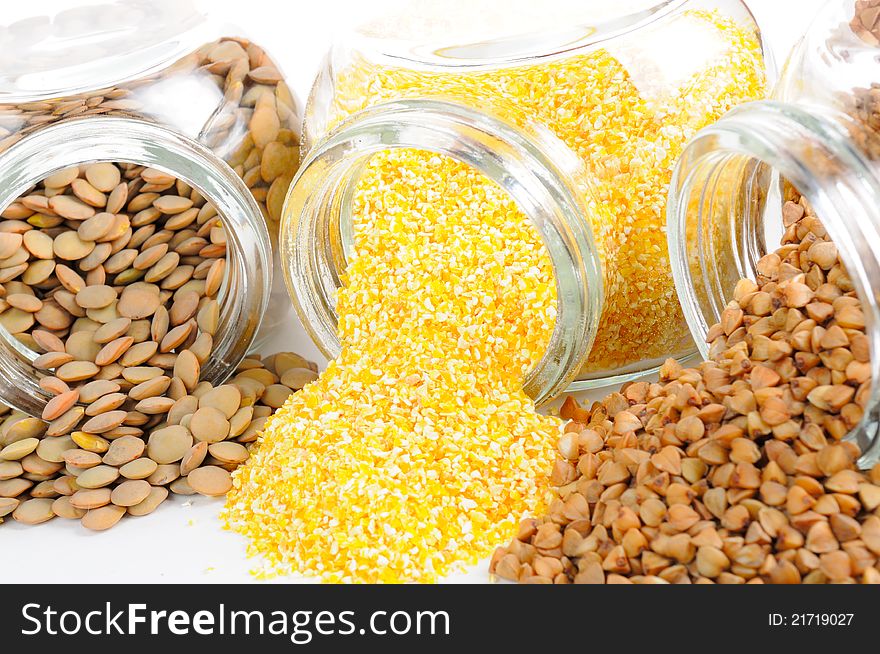 Three open glass jars with lentils, corn grits and buckwheat