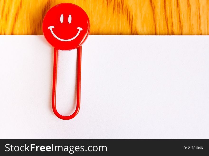 Close up of a red paper clip and white paper on wood table