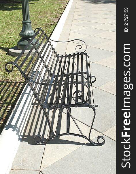 This is a black steel bench outside in a sunny day of summer.