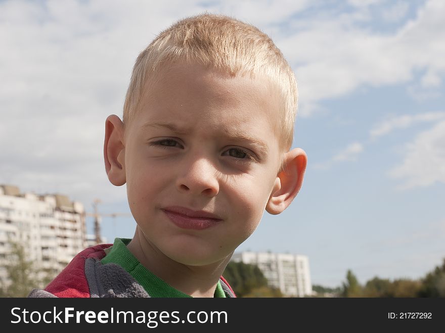 The boy of five years against the sky and buildings poses for a portrait. The boy of five years against the sky and buildings poses for a portrait