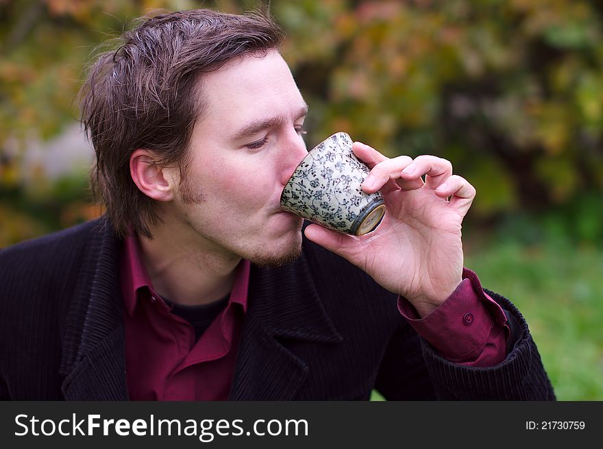 Handsome man drinking tea outdoors, the autumn background