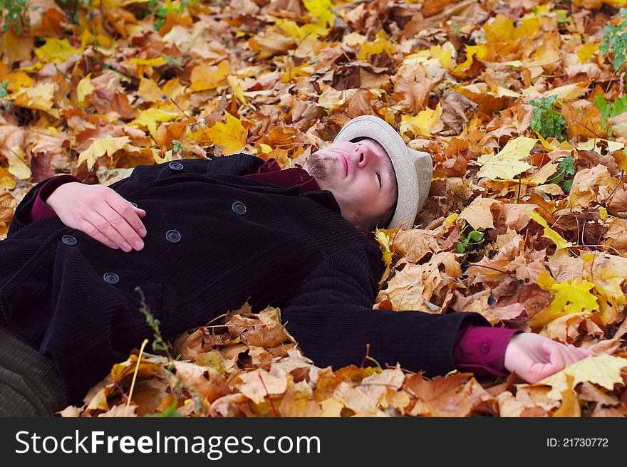 Handsome man with hat lying in autumn leaves background. Handsome man with hat lying in autumn leaves background
