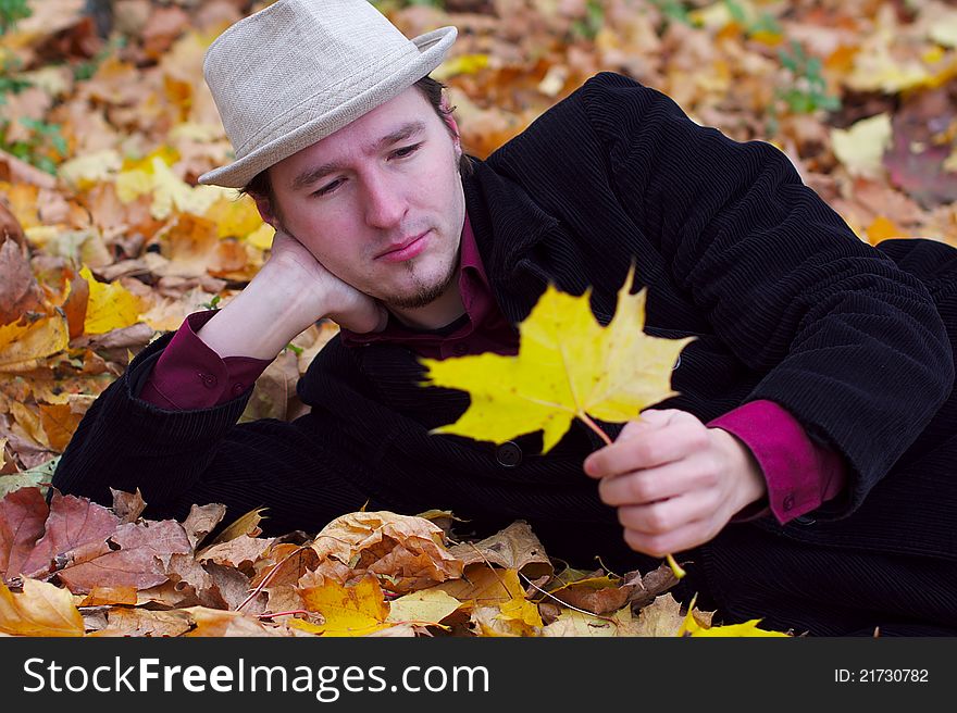 Handsome man with hat lying in autumn leaves and holding one leave. Handsome man with hat lying in autumn leaves and holding one leave