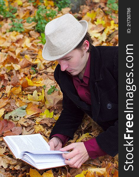 Man with a hat reading a book in autumn leaves background. Man with a hat reading a book in autumn leaves background