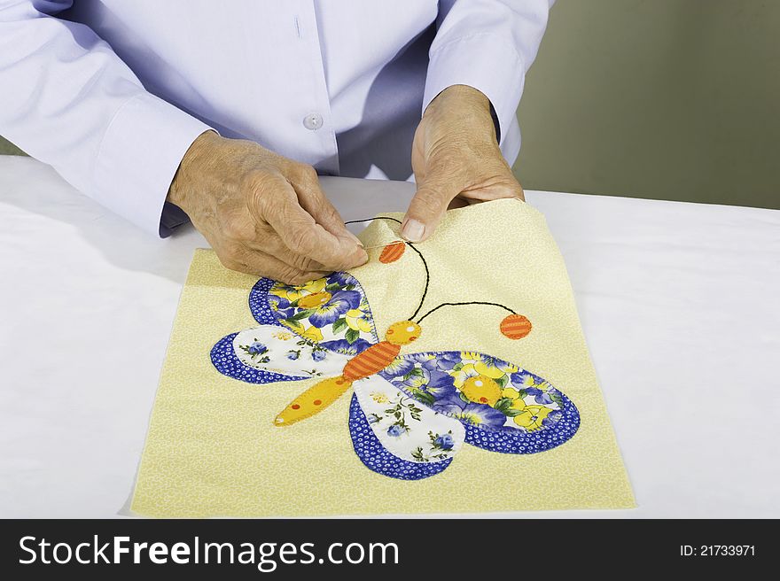 A woman stitches black thread to a quilt panel of a butterfly. A woman stitches black thread to a quilt panel of a butterfly.