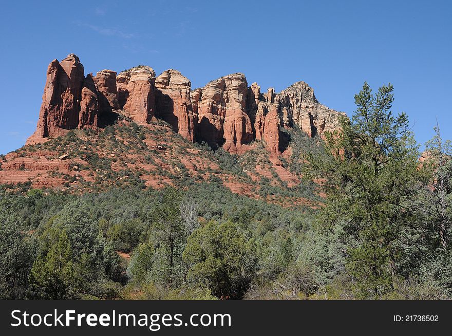Looking at a rock ledge in Sedonna Arizona, red rock pillars with blue sky, and low grass and greens near the base
