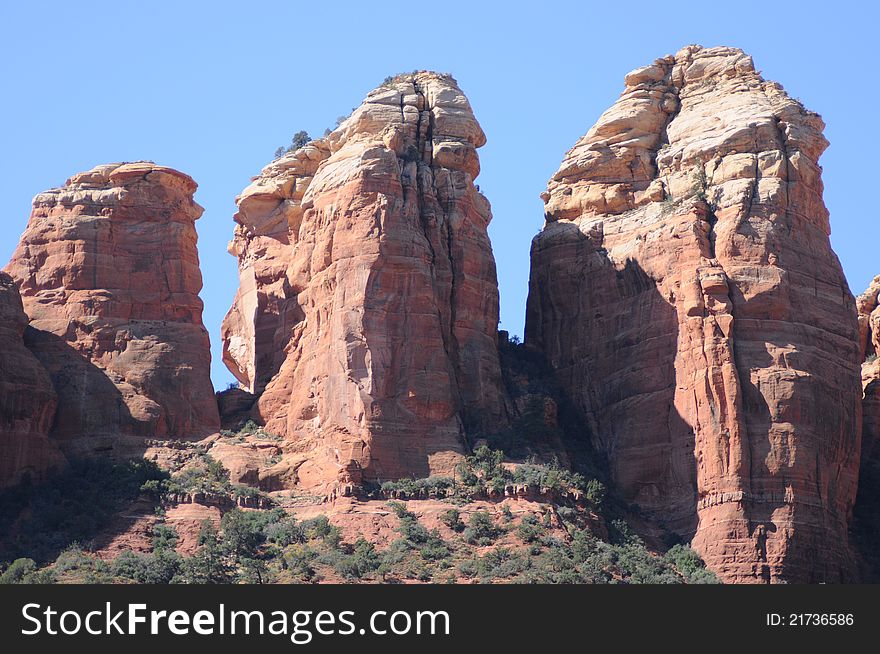 View of pillars of stone in Sedonna Arizona, gradient colors of stone, red rocks at the base and pale white at the summits, low shrub bush on the base. View of pillars of stone in Sedonna Arizona, gradient colors of stone, red rocks at the base and pale white at the summits, low shrub bush on the base