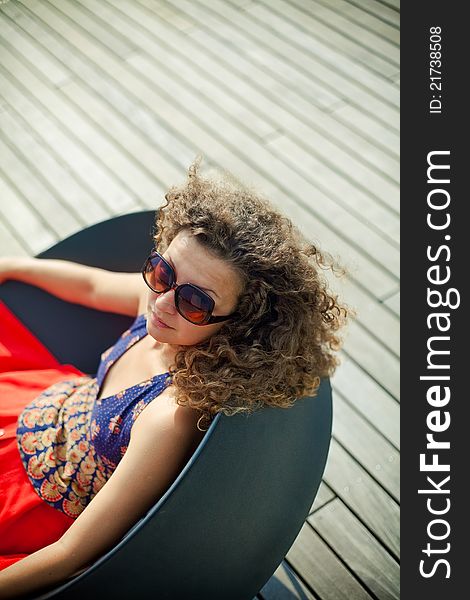 Young woman wearing sunglasses resting in a black chair. Young woman wearing sunglasses resting in a black chair