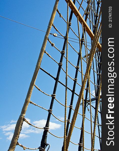 Marine rope ladder at pirate ship. Sea hemp ropes on the old nautical vessel. Ladder upstairs on the mast. Sailing ship detail at blue sky background.