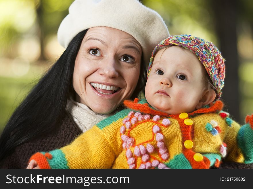 Happy mother holding her daughter in the park and watching leaves falling from the trees. Outdoor picture of a happy mom teaching her child first lessons
