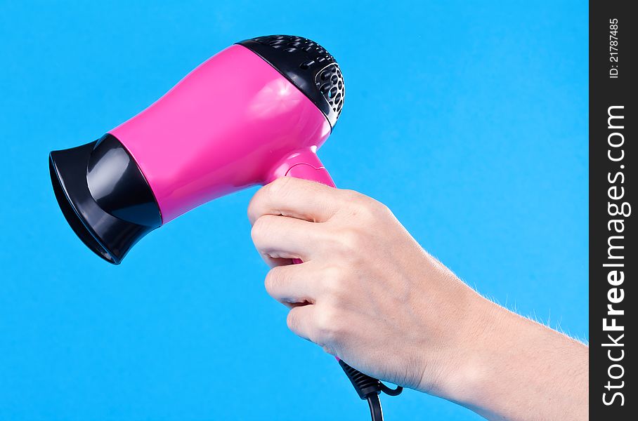 Pink hair dryer in the female hand on a blue background