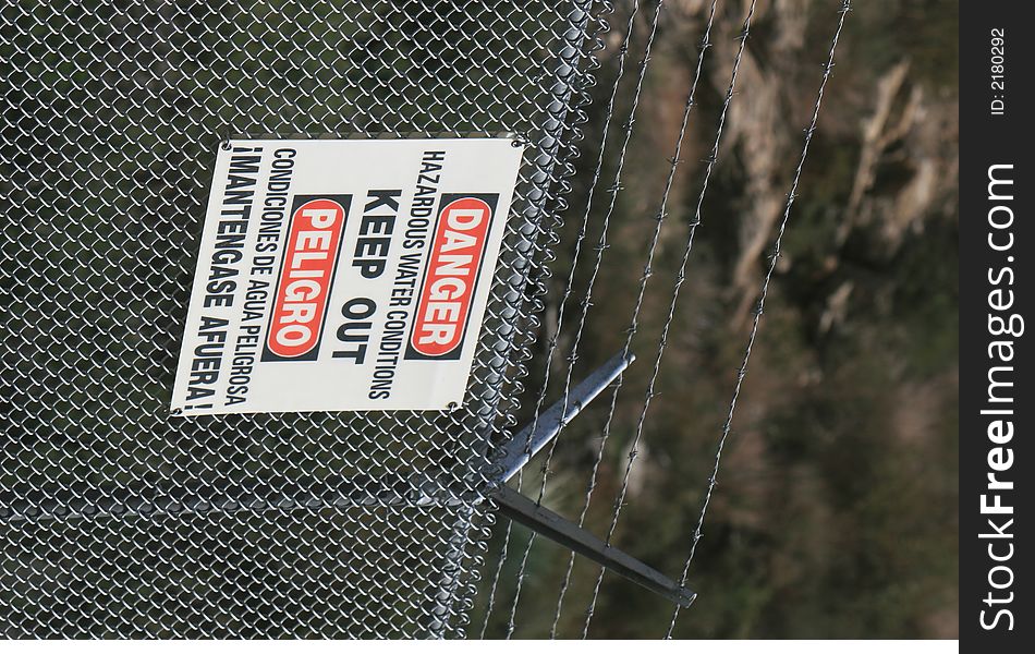 A sign warns of hazardous water conditions on a barbed wire fence. A sign warns of hazardous water conditions on a barbed wire fence