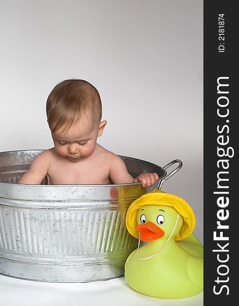 Image of cute baby sitting in a galvanized tub in front of a white background, with a large rubber duck next to it. Image of cute baby sitting in a galvanized tub in front of a white background, with a large rubber duck next to it
