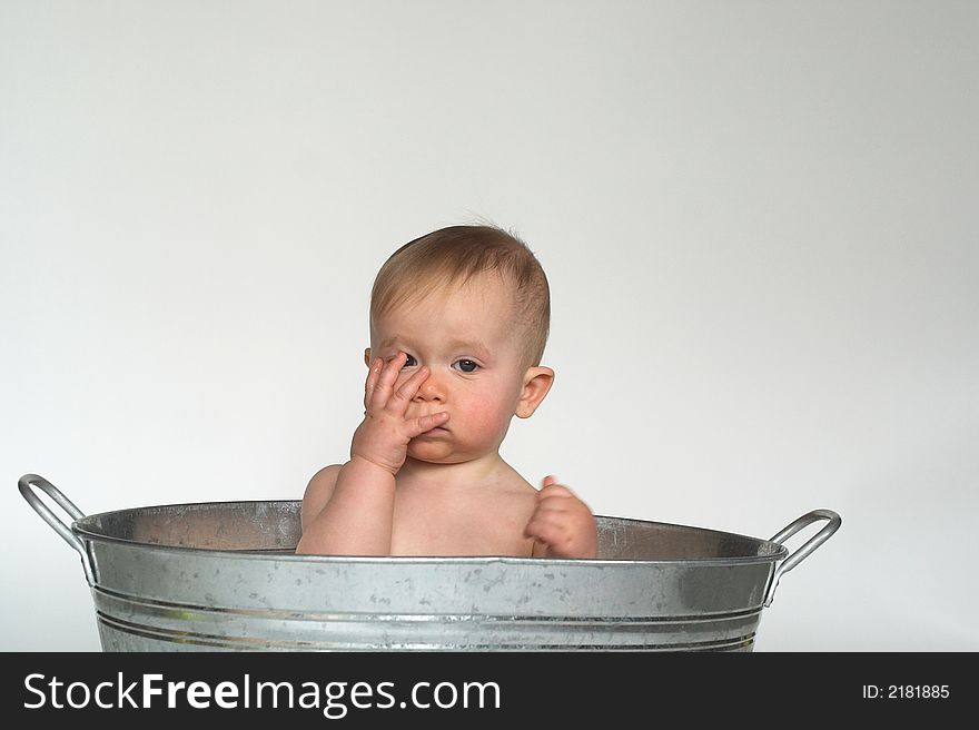 Image of cute baby sitting in a galvanized tub in front of a white background, holding a hand over his face. Image of cute baby sitting in a galvanized tub in front of a white background, holding a hand over his face