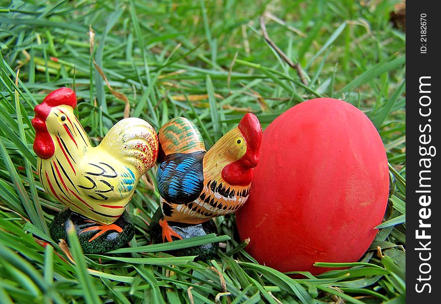 Two Chickens with red easter egg on the grass