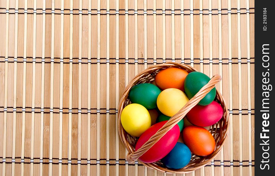 A woven basket with multi colored eggs on the reed napkin. A woven basket with multi colored eggs on the reed napkin