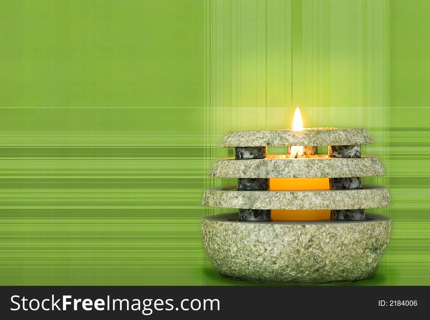 Votive candle burns in stone holder against green line patterned background. Votive candle burns in stone holder against green line patterned background