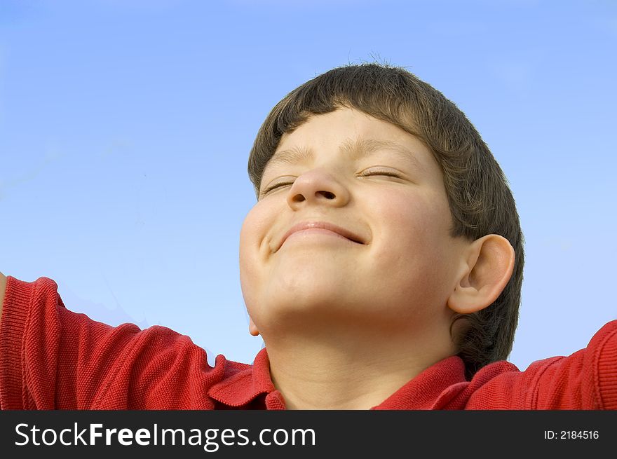 A close-up of a smiling boy tilting his head back against a blue sky and closing his eyes in pleasure. A close-up of a smiling boy tilting his head back against a blue sky and closing his eyes in pleasure.