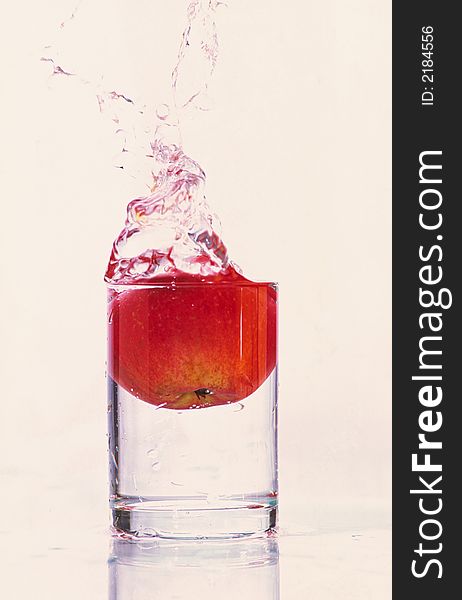 Composition from falling red apple in glass with water on white background. Composition from falling red apple in glass with water on white background