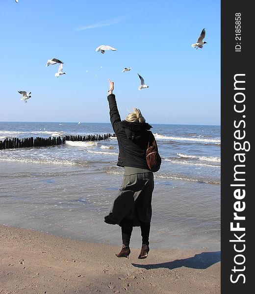 Young woman feeding seagulls on the beach in KoÅ‚obrzeg (Poland)