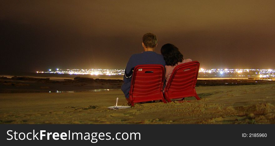 Romatic photo of couple sitting on beach, with citylights in the background. Romatic photo of couple sitting on beach, with citylights in the background.