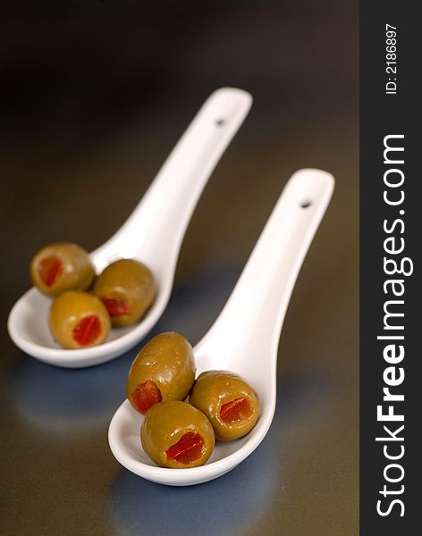 Green stuffed olives in two white spoons vertical view