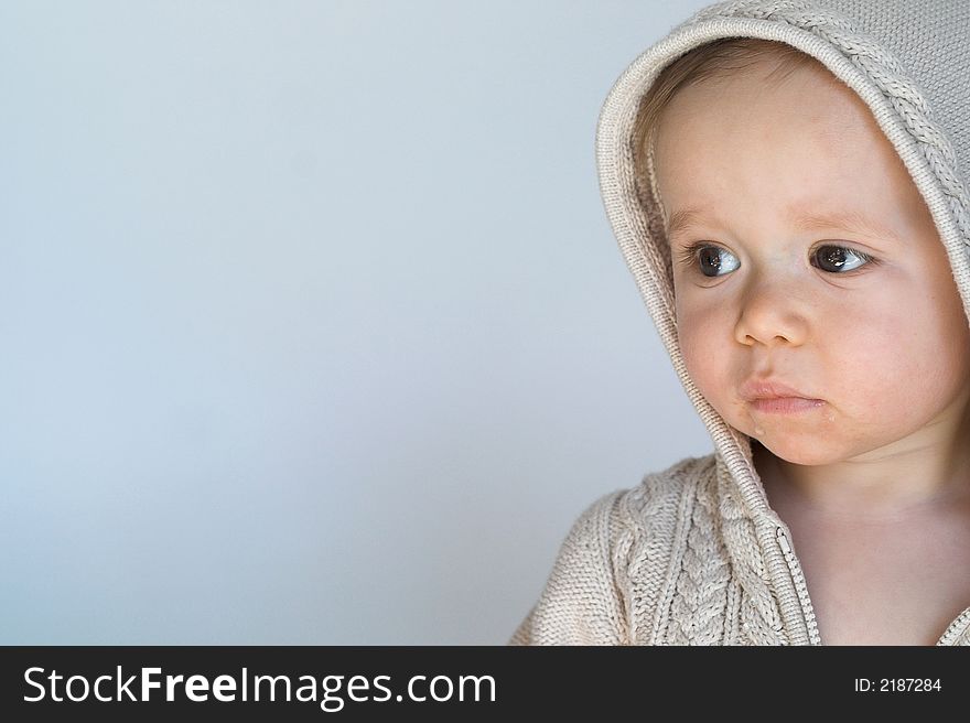 Image of cute baby wearing a hooded sweater, sitting in front of a white background. Image of cute baby wearing a hooded sweater, sitting in front of a white background