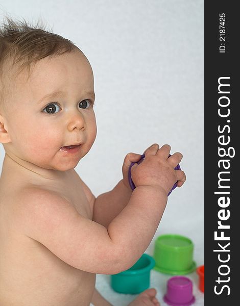 Image of adorable baby playing with stacking cups, sitting in front of a white background. Image of adorable baby playing with stacking cups, sitting in front of a white background