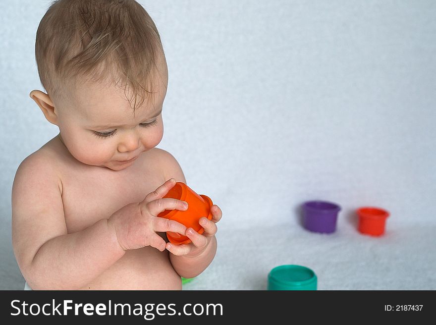 Image of adorable baby playing with stacking cups, sitting in front of a white background. Image of adorable baby playing with stacking cups, sitting in front of a white background