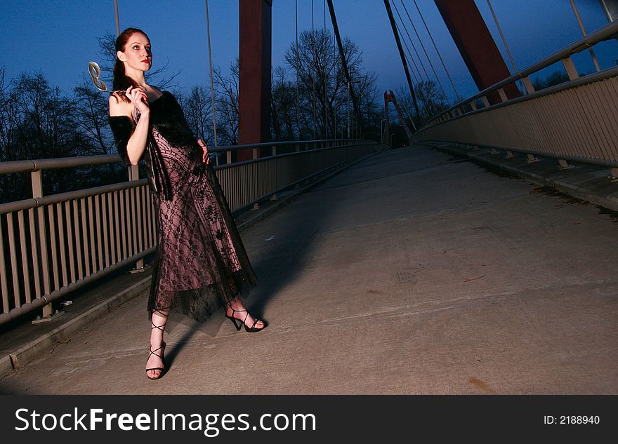 Tall female fashion model poses on a walkway at twilight. Tall female fashion model poses on a walkway at twilight.