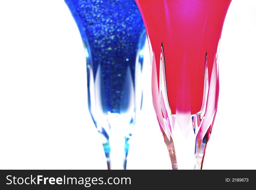 Fancy wine glasses with a swirling purple wine with sparkles in it and another glass with a bright red liquid.