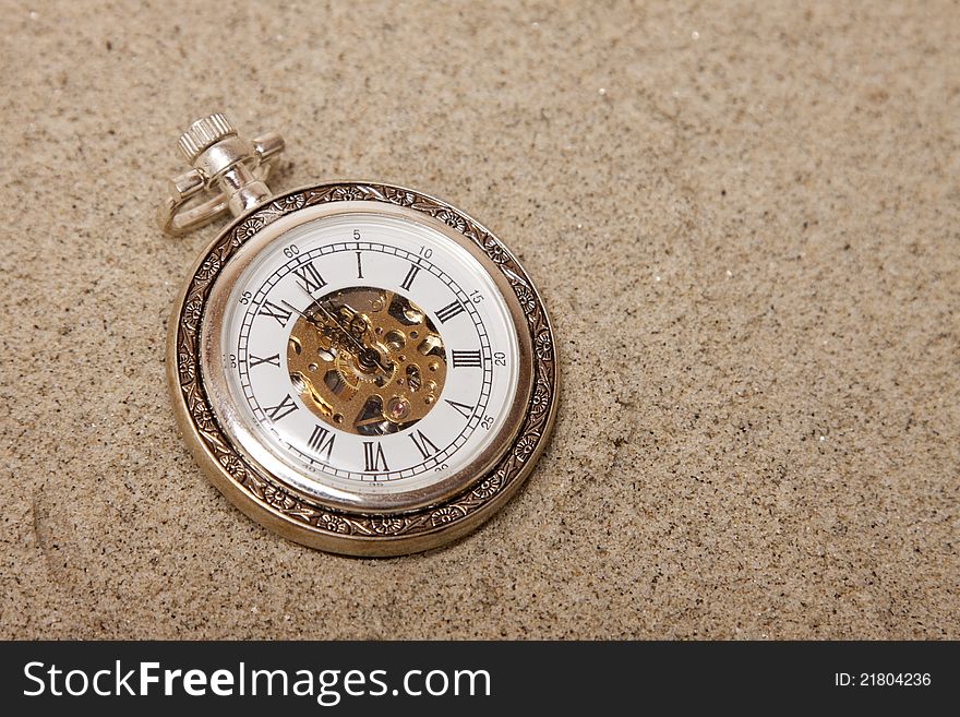 Old pocket watch buried in sand. Lost time concept.